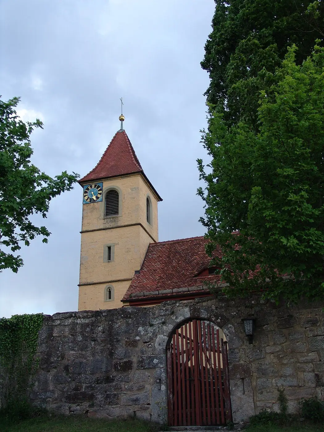 Das hölzerne Tor in der alten Friedhofsmauer vor dem Kirchturm von St. Maria und Michael in Kirnberg